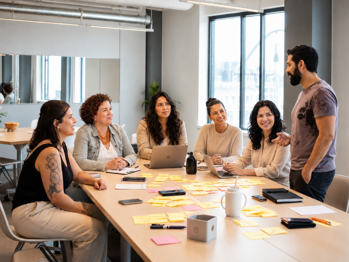 Equipe reunida ao redor de uma mesa em workshop interno com post-its e facilitador em pé